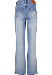 Jeans evazați din denim bleu deschis, cu o textură netedă, având o etichetă din piele maro și două buzunare spate cu detalii ale unui logo alb.