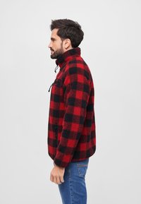 Rød og sort ternet fleece-pullover med høj krave, lynlås-lomme og afslappet pasform. Har en struktureret, blød overflade.