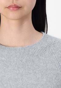 Hellgrauer gestrickter Pullover mit einem gerippten Rundhalsausschnitt und weicher Textur. Der Stoff wirkt dick und gemütlich, mit einem dezenten Muster.