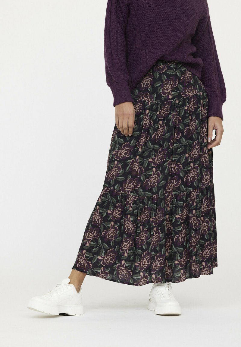 Jupe maxi florale avec un fond vert foncé et des roses violettes, design en étages et tissu doux, portée avec des baskets blanches.