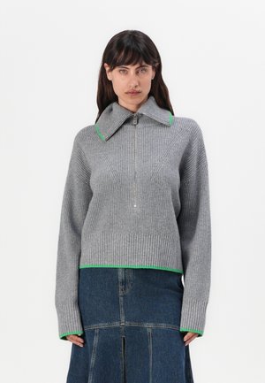 Suéter de punto gris con un alto cuello con acentos verdes, textura acanalada y diseño de media cremallera. Largo cropped y mangas largas.