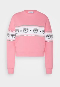 Sudadera corta rosa hecha de tela suave que presenta una banda gráfica blanca con diseños de ojos y detalles plateados en el pecho y las mangas.