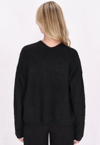 Maglione nero a maglia con scollatura a V e spalle scese. Tessuto texturizzato, vestibilità rilassata e maniche di lunghezza media. Senza motivi o dettagli visibili.