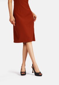 Tacchi alti neri peep-toe con finitura testurizzata e tacco a stiletto che allunga la gamba, abbinati a un vestito aderente color ruggine.