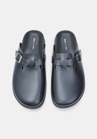 Fekete, sima műanyagból készült slip-on klumpák ezüst csat díszítéssel az elején és lekerekített orral.