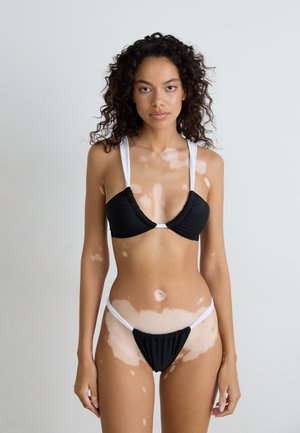 Black bikini set featuring a top with gathered cups, wide white straps, and low-rise bottoms with white accents, against a neutral background.