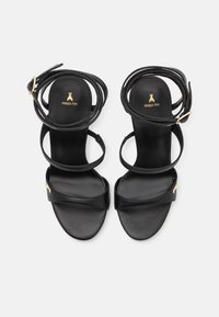 Sandales en cuir noir avec des fines lanières et une semelle plate. Accents en métal doré et logo sur la semelle intérieure. Design à bout ouvert.