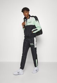 Träningsdräkt i lättviktstyg, med svart bas och mintgröna accenter. Inkluderar en jacka med dragkedja och elastiska byxor, märkesprodukter.