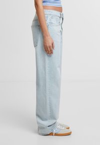 Lichtblauwe wijdlopende jeans van denim, met een hoge taille, zijzakken en een relaxte pasvorm, gecombineerd met grijze en beige sneakers.