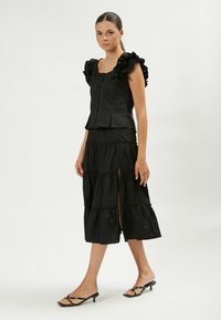 Conjunto negro de dos piezas que incluye una blusa ajustada con mangas con volantes y una falda de varios niveles hasta los tobillos con abertura lateral, hecha de tejido ligero.