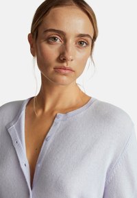 Levandulový, lehký pletený kardigan s kulatým výstřihem, zapínáním na knoflíky a texturovanou tkaninou. Jednoduchý design s jemnými detaily v prošívání.