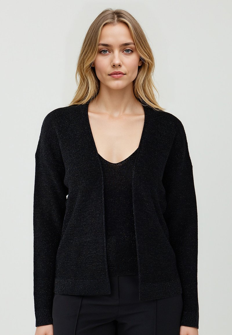 Cardigan nero con scollo a V, motivo a maglia testurizzata, apertura anteriore e vestibilità rilassata. Indossato sopra un top nero coordinato.