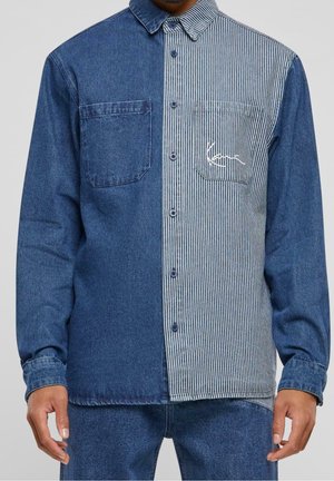 Chemise homme à manches longues boutonnée avec un design divisé : denim bleu foncé uni à gauche, rayures verticales bleues et blanches à droite, avec poches poitrine.