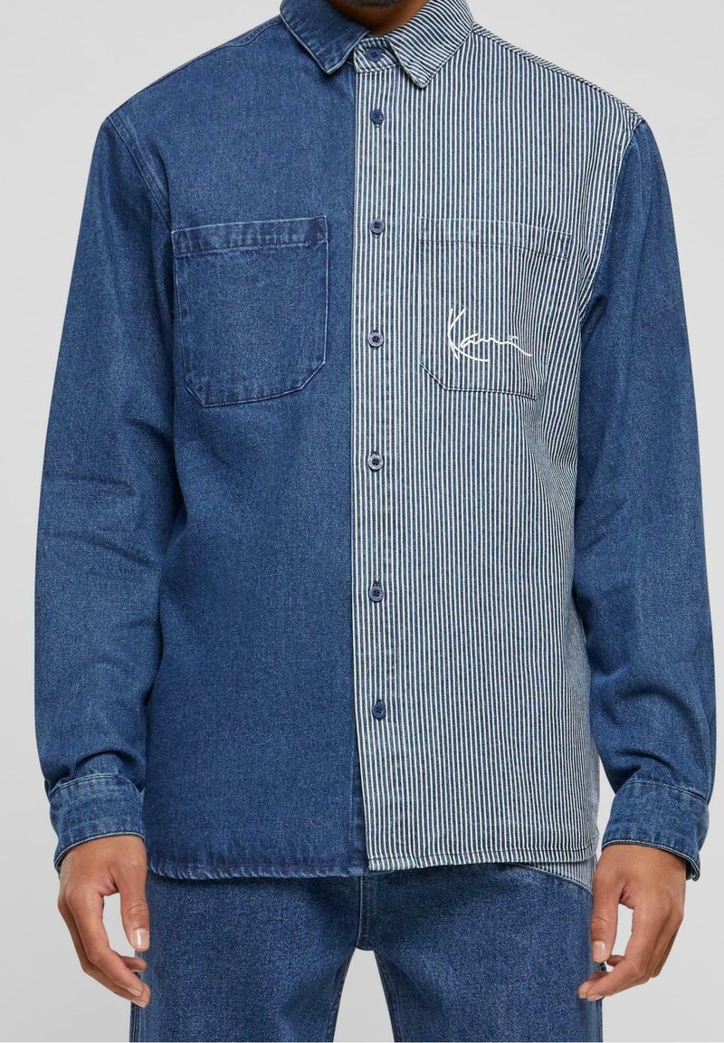 Chemise homme à manches longues boutonnée avec un design divisé : denim bleu foncé uni à gauche, rayures verticales bleues et blanches à droite, avec poches poitrine.