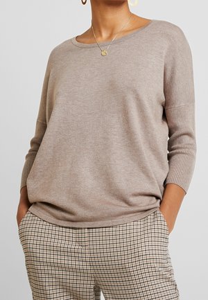Hellbraunes Strickpullover mit Rundhalsausschnitt und Dreiviertelärmel, kombiniert mit karierten Hosen. Weiche Textur und lockere Passform.