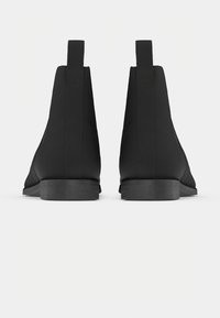 Paire de bottines Chelsea noires vues de dos avec des languettes de tirage et des talons bas empilés sur un fond neutre.
