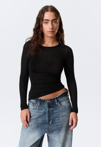 Top nero a maniche lunghe con design aderente e arricciato. Abbinato a jeans di denim azzurro chiaro, ampi. Stile semplice e minimalista.