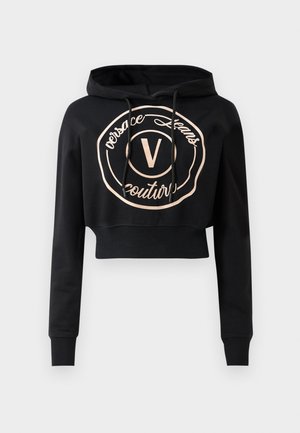 Hoodie noir court avec des manches longues, présentant un logo circulaire en rose gold et des cordons de serrage au niveau du col. Fabriqué en tissu doux.