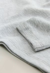 Sivý rebrovaný textil s jemnou textúrou, so sklopeným manžetovým detailom. Jednoduchý dizajn bez viditeľných vzorov alebo akcentov.