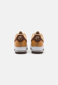 Sneakers Nike Air avec un dessus en cuir jaune et marron, une semelle intermédiaire blanche et une semelle extérieure en caoutchouc marron textur é. Marque sur le talon.
