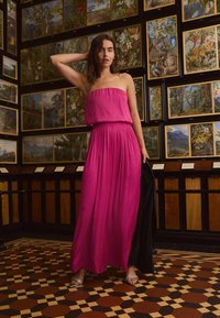 Fuchsia strapless maxiklänning med samlad midja, sl�ät textur och flödande tyg, tillsammans med silvriga remsandaler mot ett mönstrat golv.