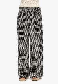 Pantalones de pierna ancha en blanco y negro con un patrón geométrico, cinturilla elástica, tela fluida y corte relajado.