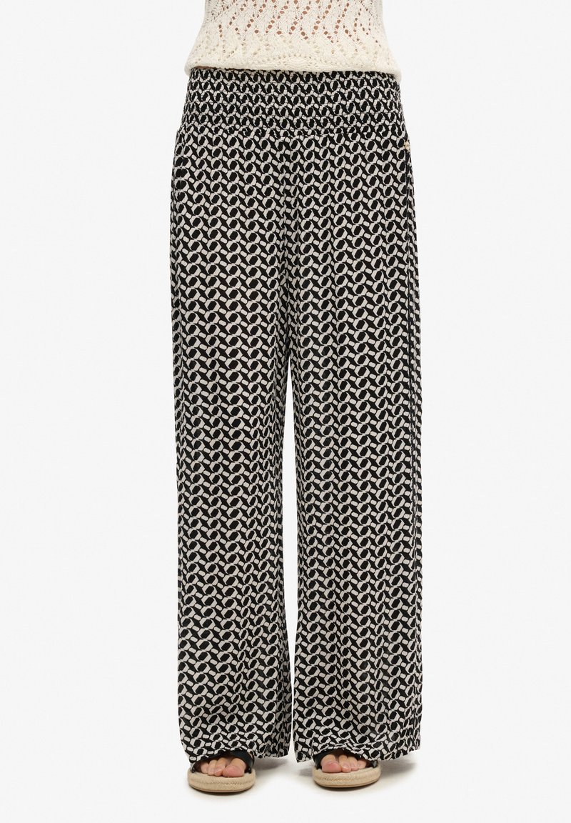 Pantalones de pierna ancha en blanco y negro con un patrón geométrico, cinturilla elástica, tela fluida y corte relajado.