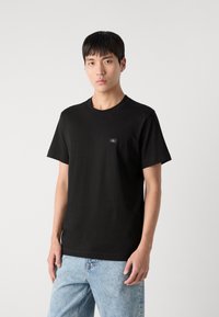 Black cotton t-shirt featuring a round neckline and short sleeves, with a small logo patch on the chest and a smooth texture.