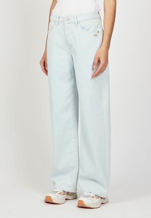 Hellblaue weit geschnittene Jeans mit hoher Taille aus Denim. Mit Zahlenfronttaschen und einem Markenetikett, kombiniert mit weißen Sneakers.