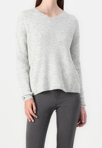 Maglione a costine grigio chiaro con scollo a V e maniche lunghe, realizzato in materiale morbido, abbinato a jeans aderenti grigio scuro.