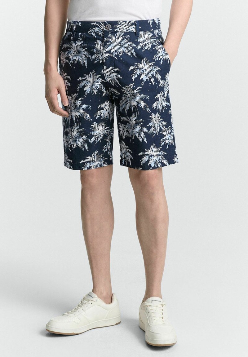 Marinefarbene Shorts mit einem weißen Palmenmuster, aus leichtem Stoff, mit geradem Schnitt und Taschen, kombiniert mit weißen Sneakers.