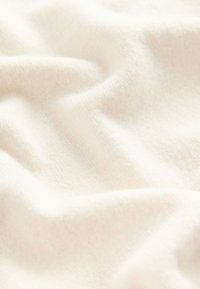 Tissu crème clair drapé avec une texture douce et lisse, présentant des variations subtiles de teinte et un motif fin, tricoté discrètement.