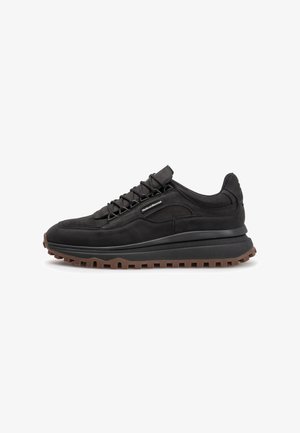Black sneakers with a textured suede and mesh upper, ridged rubber outsole, and lace-up design. Features a discreet brand label on the side.