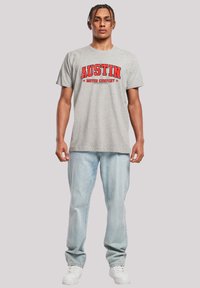 Gray cotton t-shirt with red "AUSTIN MOTOR COMPANY" graphic. Paired with light blue jeans and white sneakers.