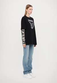 Svart oversized t-skjorte med grafisk design av et løvehode, kombinert med en langermet topp med zebra-mønster, lyseblå jeans og hvite joggesko.