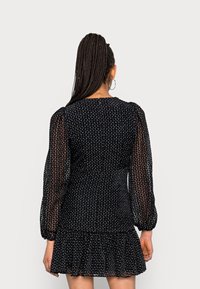 Robe noire avec un corsage texturé, des manches flottantes et transparentes, et un ourlet à volants. Présente une silhouette ajustée et des détails subtils ressemblant à des perles.