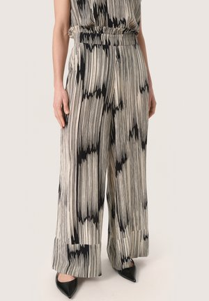 Black and white patterned wide-leg pants with a textured finish. Elastic waistband and hemmed cuffs. Worn with pointed black flats.
