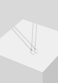 To sølvhalskæder med delte hjertevedhæng. Kæderne er delikate og har et klassisk design, afsluttet med en poleret overflade.