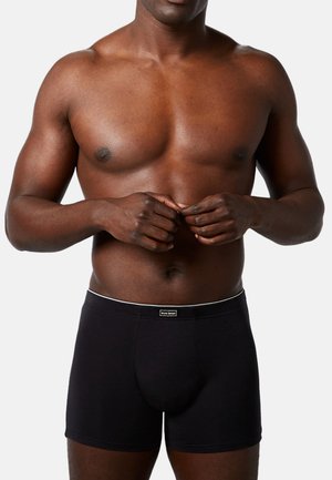 Schwarze Boxer-Briefs mit einem weißen Bund und Branding. Weicher Stoff, figurbetonte Passform und ein konturiertes Vorderdesign für zusätzlichen Halt.