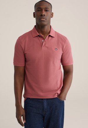 Roze polo shirt met kraag, korte mouwen en een klein embleem op de borst, gecombineerd met donkere spijkerbroek.