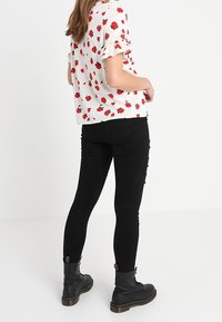 Blusa blanca con flores y rosas rojas, mangas cortas con volantes, combinada con pantalones skinny negros de cintura alta y botas negras con cordones.