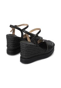 Sandalias de cuña negras con detalles de yute trenzado, correas ajustables y un acabado de cuero suave. Diseño de punta cerrada con un ligero acolchado.