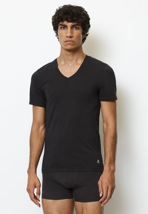 Schwarzes V-Ausschnitt-T-Shirt aus weichem Material, mit kurzen Ärmeln, figurbetontem Design und kleinem Logo auf der unteren linken Seite, kombiniert mit schwarzer Unterwäsche.