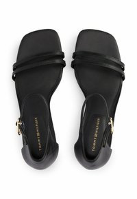 Sandali neri con suola piatta, dotati di due cinture sottili sulla parte superiore e una parte posteriore aperta. Dettagli in oro su un lato.