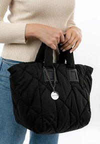 Black quilted tote bag with two fabric handles and a silver chain accent. Features a square tag and a soft texture.