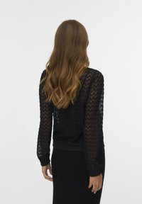 Black lace sweater with textured pattern and ribbed cuffs, paired with a smooth black skirt, viewed from the back.