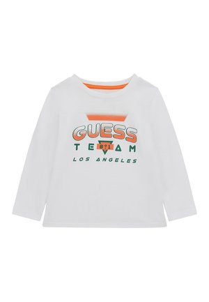 Chemise blanche à manches longues avec texte "GUESS TEAM Los Angeles" orange et vert et un petit graphique en forme de triangle orange sur le devant.