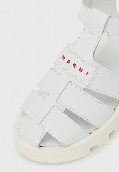 Λευκό δερμάτινο σανδάλι με φαρδιές λωρίδες με κοψίματα και κλείσιμο με βέλκρο, που εμφανίζει κόκκινο λογότυπο "MARNI" στην κορυφή.