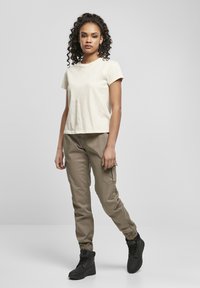 T-shirt a maniche corte beige chiaro abbinato a pantaloni cargo verde oliva con tasche laterali e stivali neri alla caviglia con finitura testurizzata.
