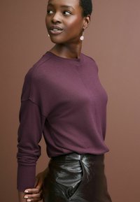 Maglione a maglia di un profondo viola con polsini a costine, abbinato a una gonna in pelle nera lucida. Design semplice, che mette in risalto un collo rotondo e una morbida texture.